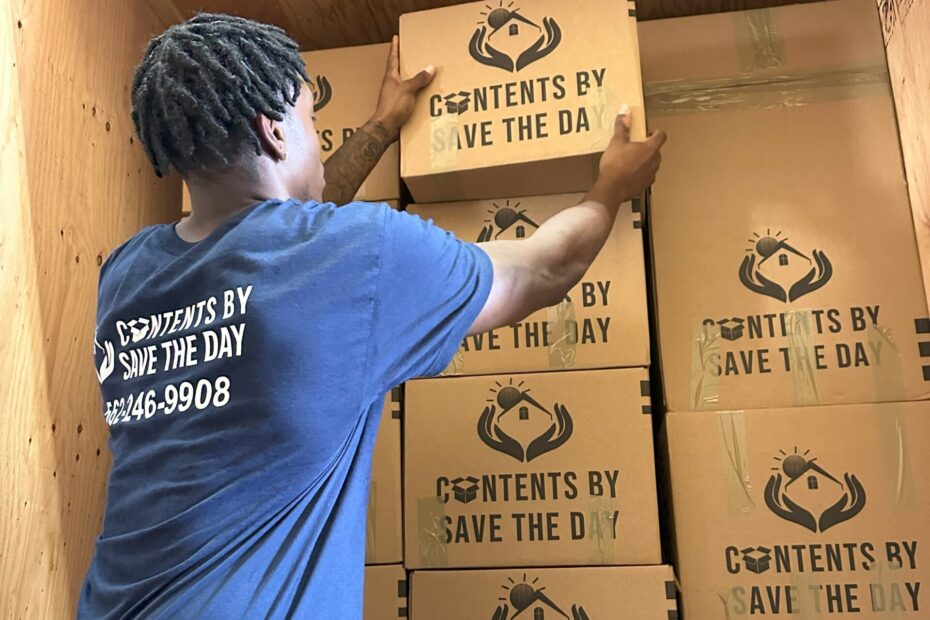 Technician from Contents by Save The Day carefully stacking branded boxes in a wooden storage unit. Have any Contents Restoration FAQ? Contact Us Today!