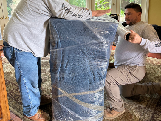 Team members shrink wrapping furniture for secure transport in the pack-out process